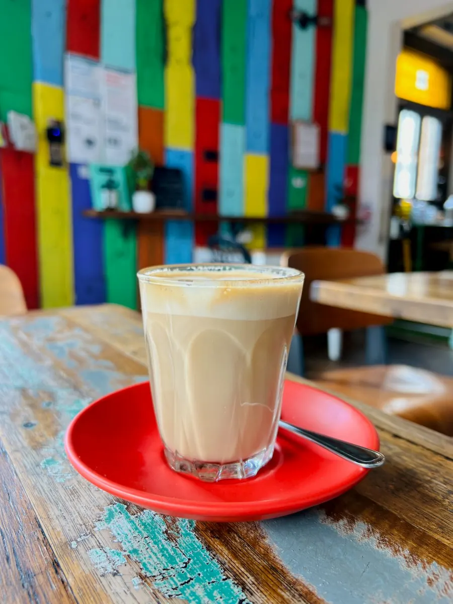 Milchkaffee auf rotem Unterteller vor bunter Café-Wand
